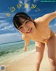 A woman in a yellow bikini standing on a beach.