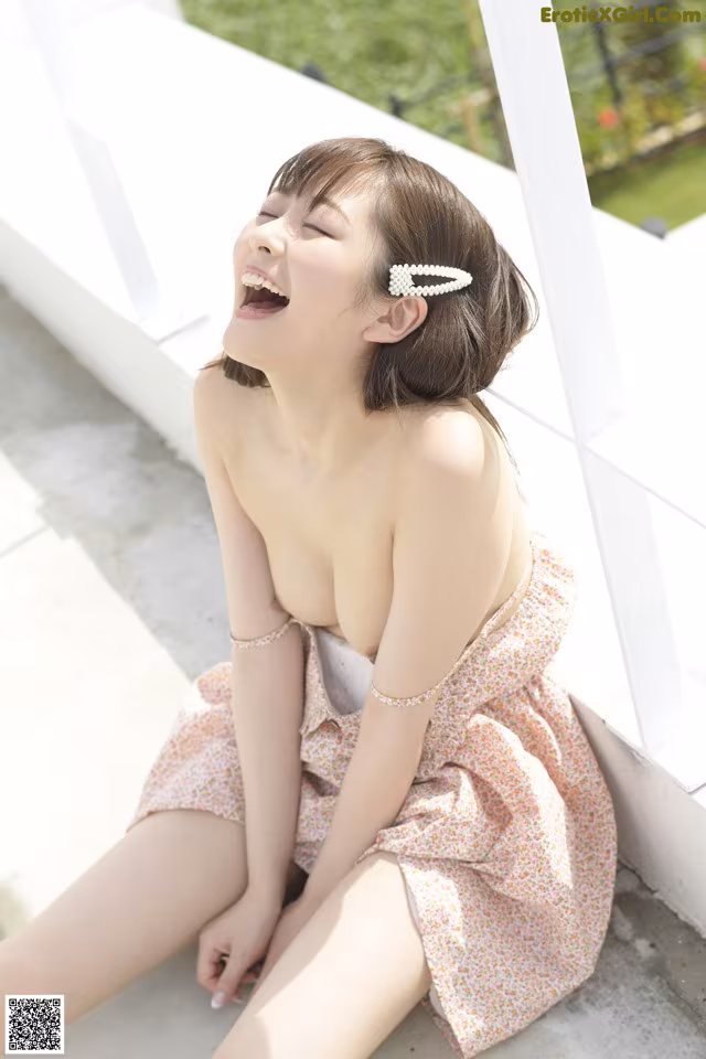 A woman sitting on the ground laughing and wearing a pink dress.