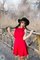 A woman in a red dress and black hat posing for a picture.