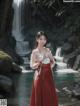 A woman in a red dress standing in front of a waterfall.