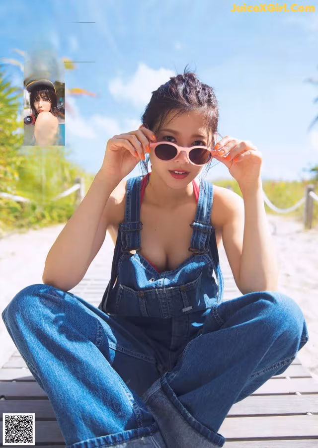 A woman sitting on a wooden dock wearing overalls and sunglasses.
