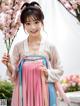 A woman in a pink and blue hanbok holding a flower.