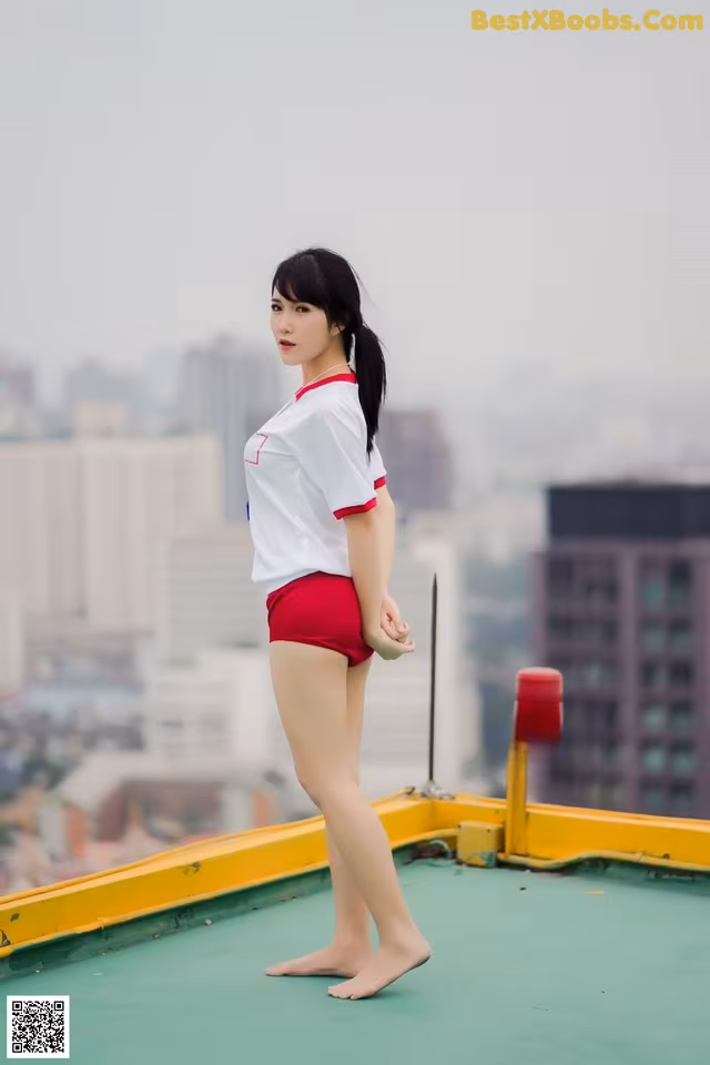 A woman in a white shirt and red shorts standing on top of a building.