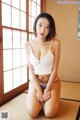 A woman in a white bikini sitting on a tatami mat.