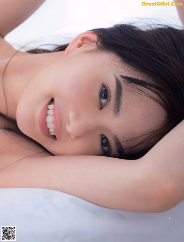 A woman laying on top of a bed with her hands behind her head.