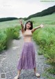 A woman standing on a gravel road with her arms outstretched.