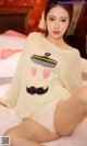 A woman sitting on a bed wearing a sweater with a mustache.