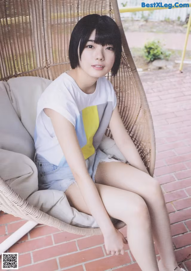 A woman sitting in a wicker chair on a brick patio.