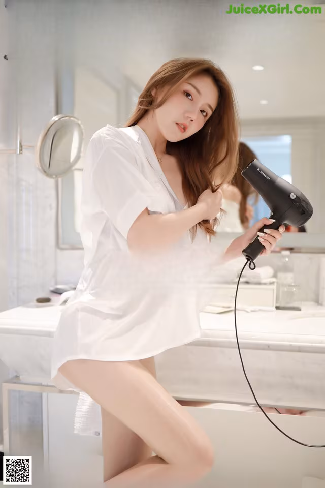 A woman in a white shirt is holding a hair dryer.